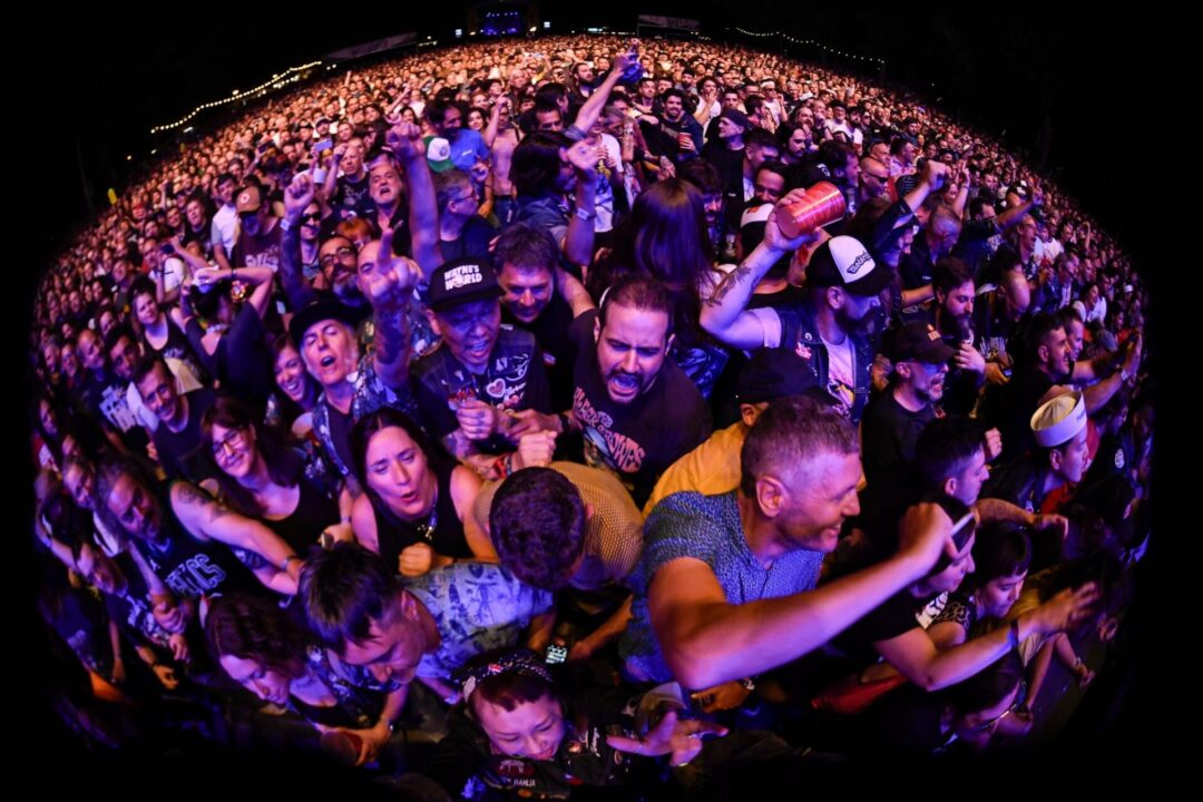 Público del Azkena Rock Festival abarrotando la primera fila de un concierto, cantando y levantando los brazos.