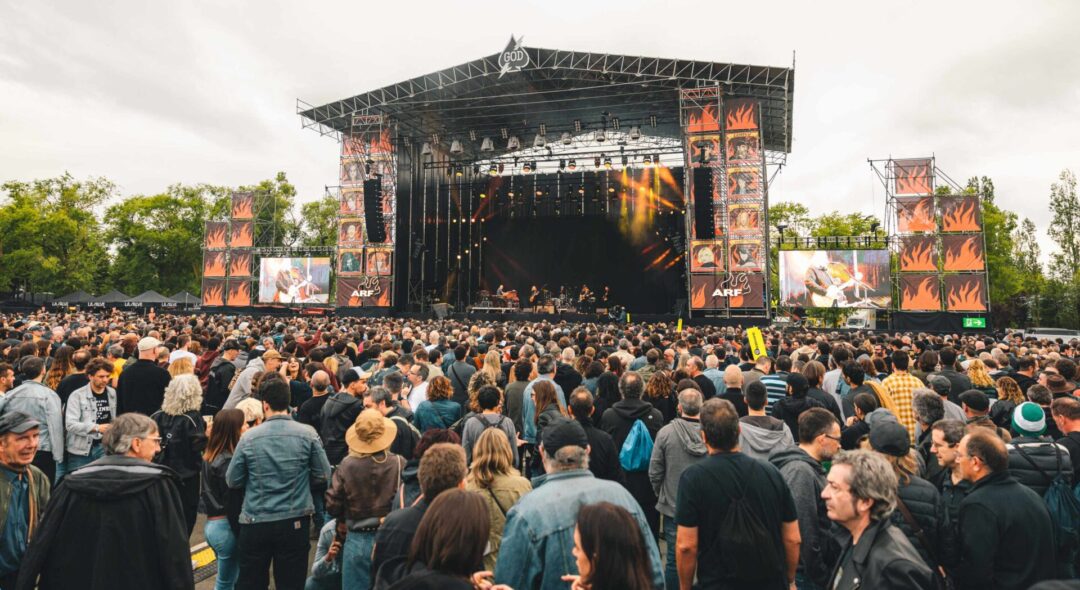 Escenario principal del festival con pantallas gigantes y decoraciones de llamas, rodeado de una multitud disfrutando del concierto.