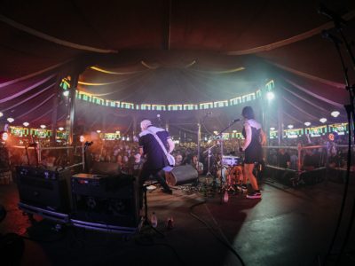 Banda actuando en el escenario de Trashville, el espacio temático del Azkena Rock Festival, con público disfrutando del ambiente íntimo y decorado con vidrieras y luces cálidas.